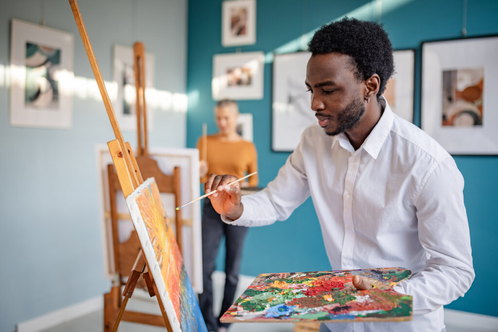 A man painting on canvas in front of an easel.