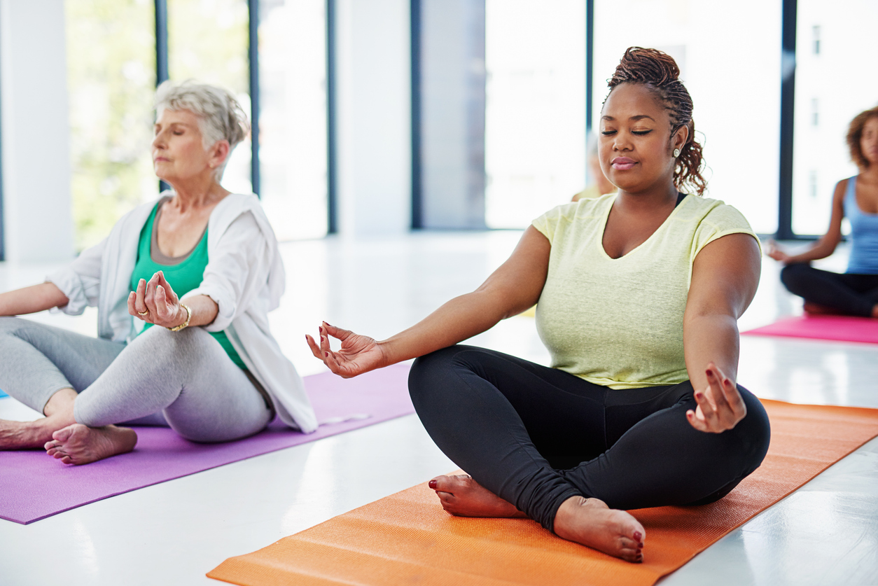 Two women sitting on a yoga mat in the middle of an exercise class.
