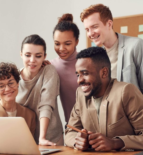 A group of people sitting around a table looking at a laptop.